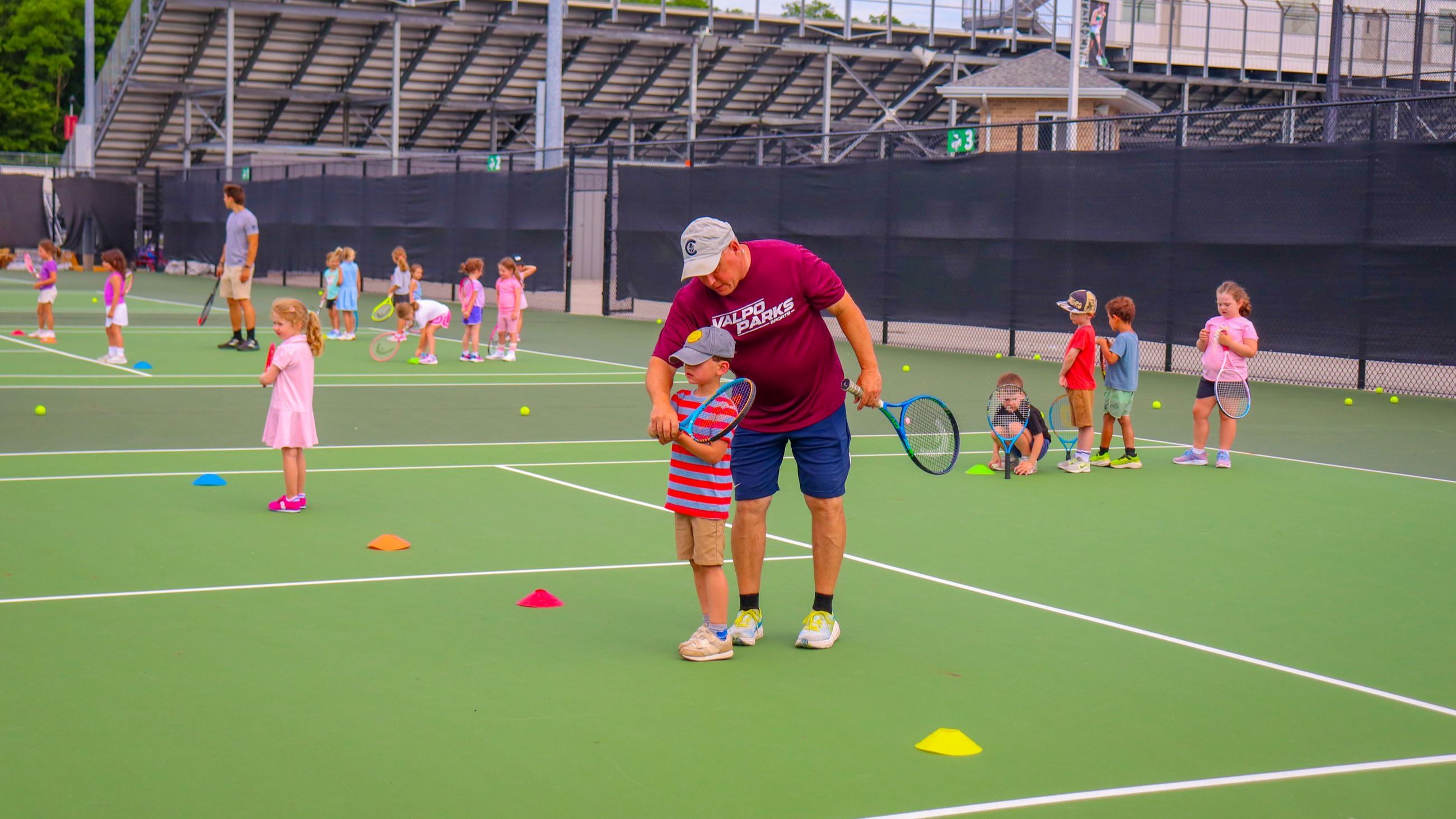 A coach helping a kid swing a tennis racket