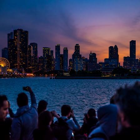 Photo of the Chicago skyline from the water, in the evening, with onlookers in the foreground.
