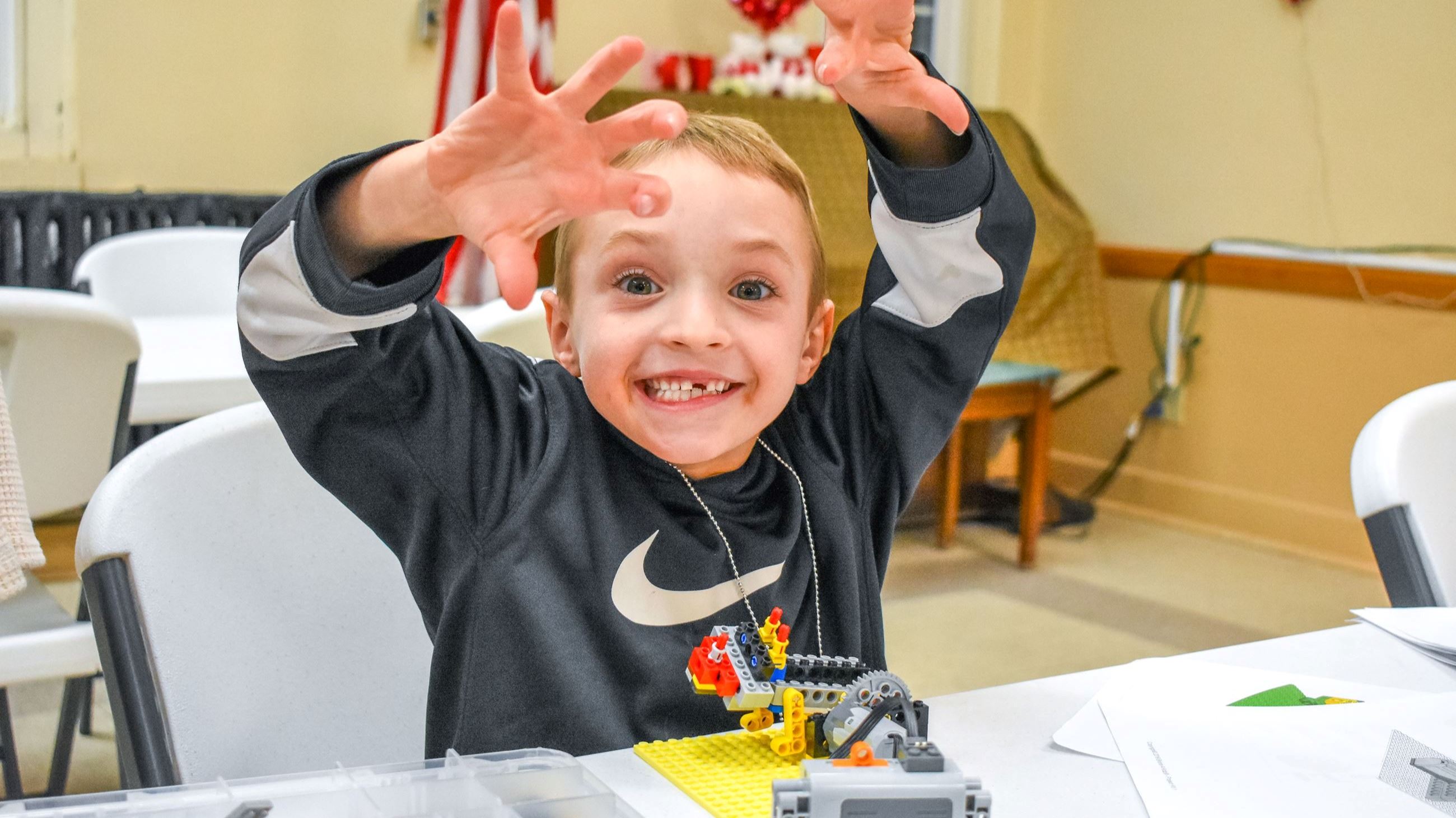 Boy holding up legos and smiling towards a camera